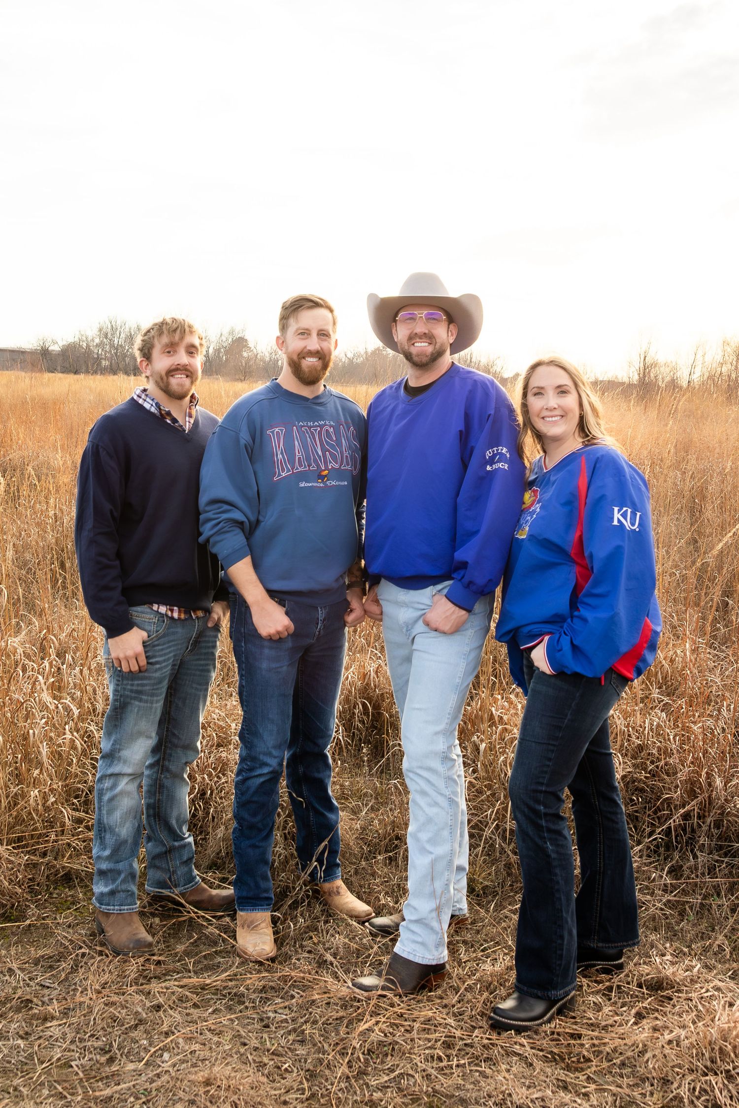 Group of people standing together in a field of tall dried grass during golden hour.