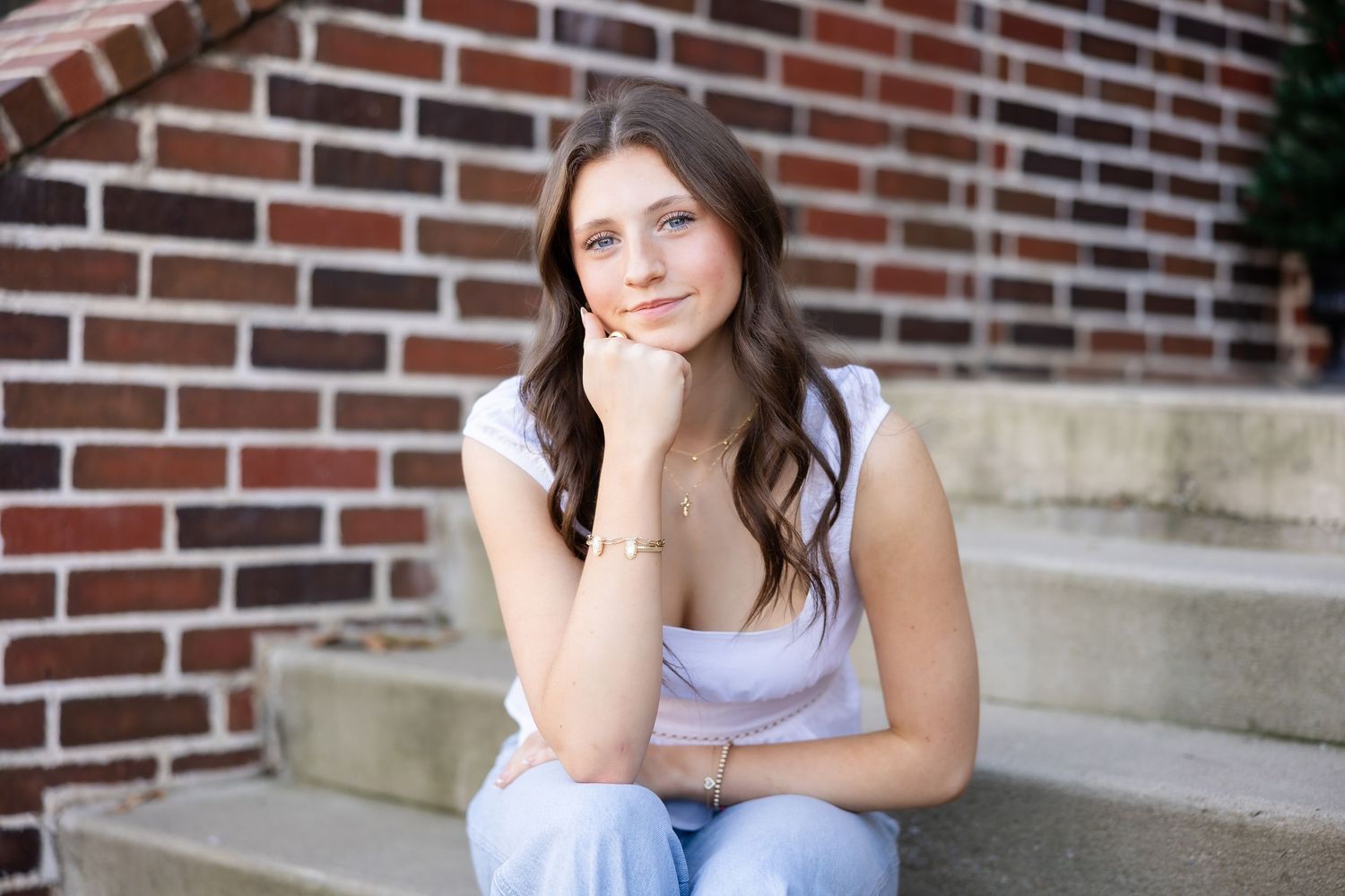 A person in a white tank top sits on brick steps outside a building in multiple poses.