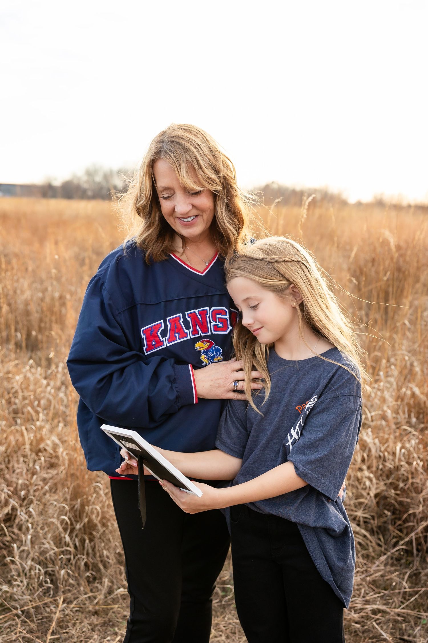 Two people in navy blue sweatshirts share a warm embrace while looking at a phone in an autumn field.