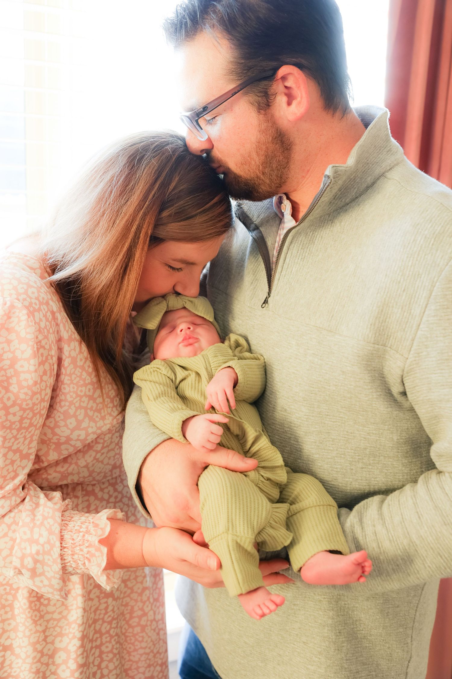 A couple shares an intimate moment while holding their newborn baby in a green onesie.