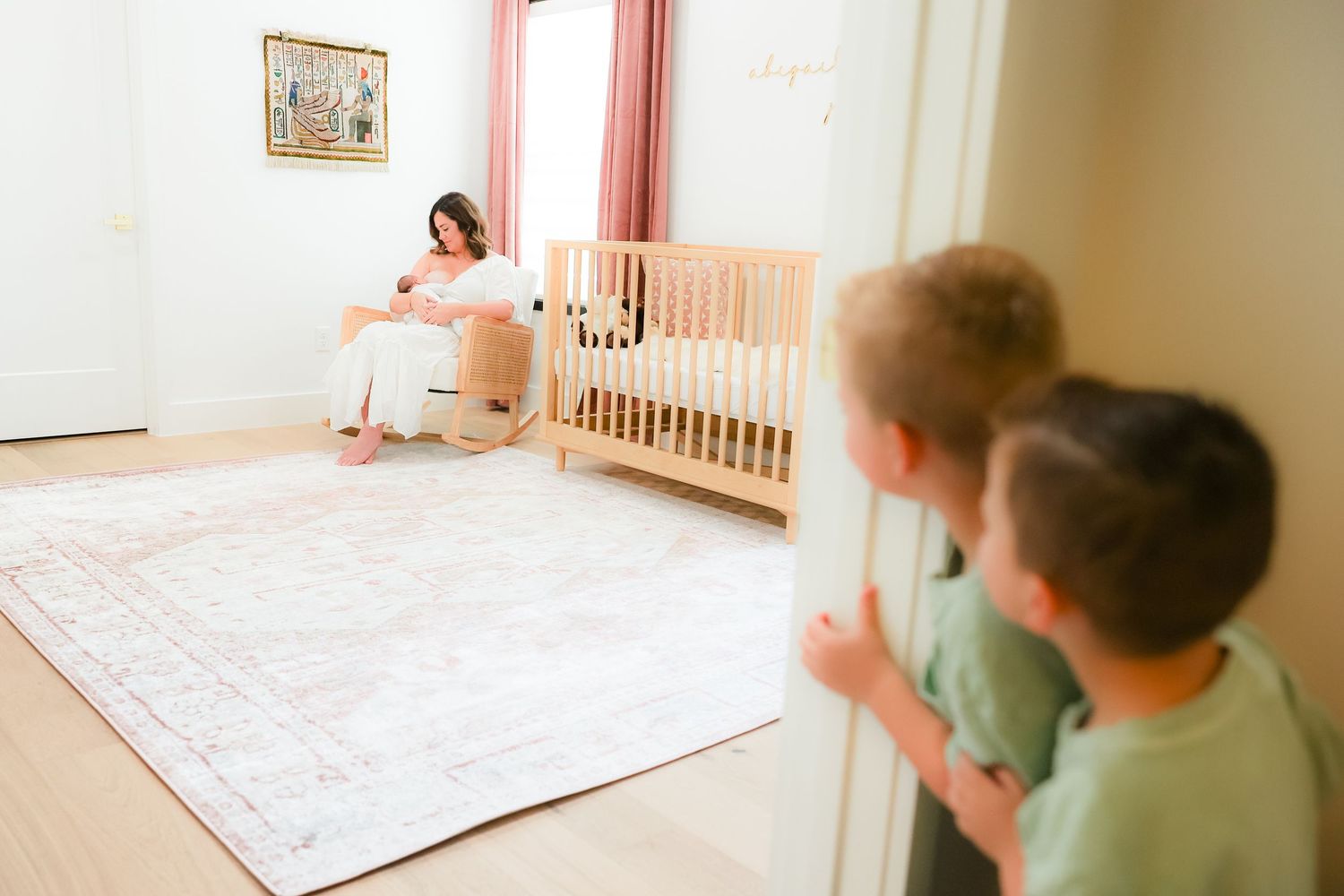 Children peek into a room where a crib and area rug can be seen in a minimalist nursery setting.