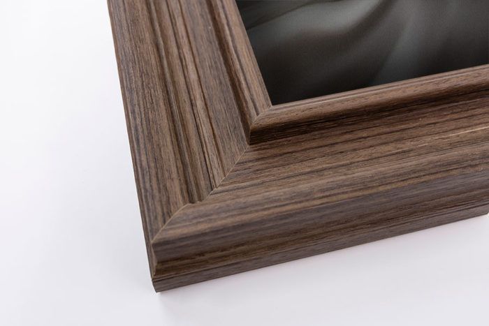 Close-up of a dark walnut wood picture frame corner with elegant ridged molding detail.