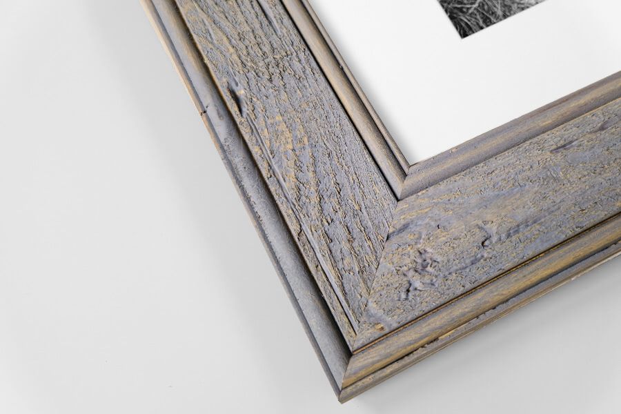 Gray weathered barnwood picture frame corner with white mat and photo on white background.