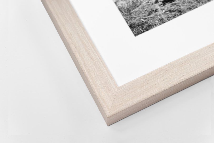 Light natural wood grain picture frame corner with white mat and black and white photograph.