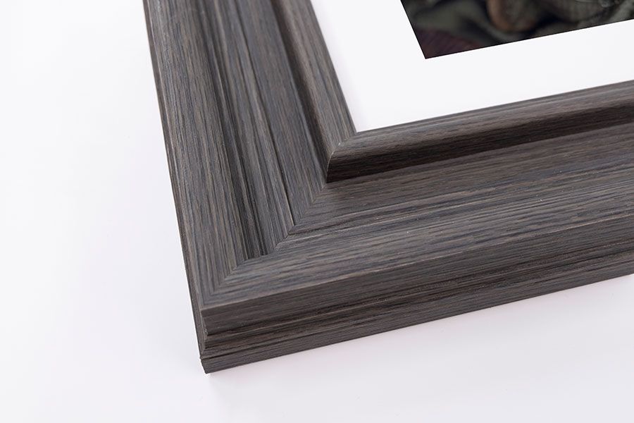 Dark gray wood grain picture frame corner with white mat and photo on white background.