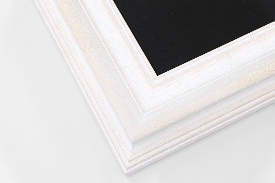 Distressed white wood ornate picture frame corner with layered molding and black canvas backing.