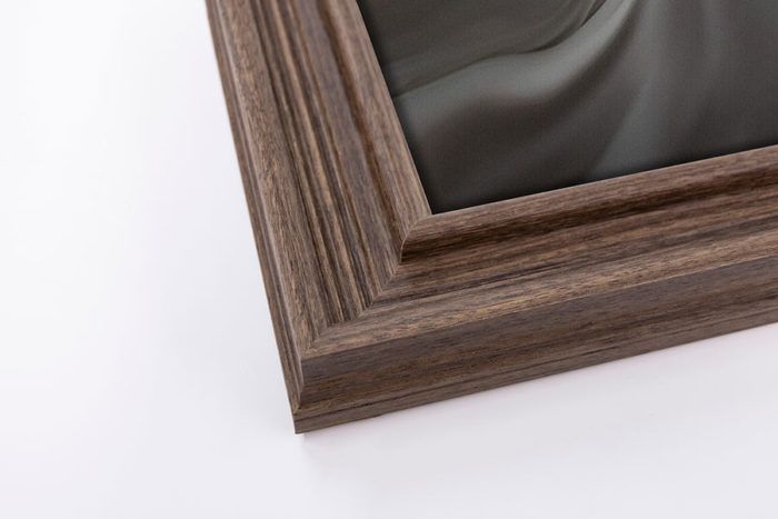 Close-up corner detail of a warm walnut brown wood picture frame on a white background.
