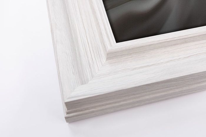 Close-up of a white distressed wood picture frame corner with layered molding detail.