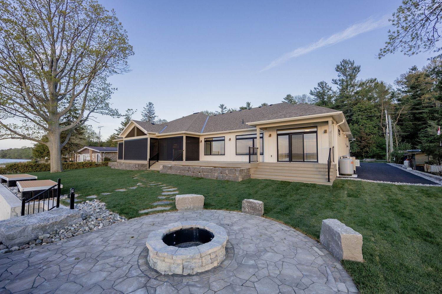 Ranch home backyard with stone fire pit, stamped concrete patio, screened porch, and green lawn.