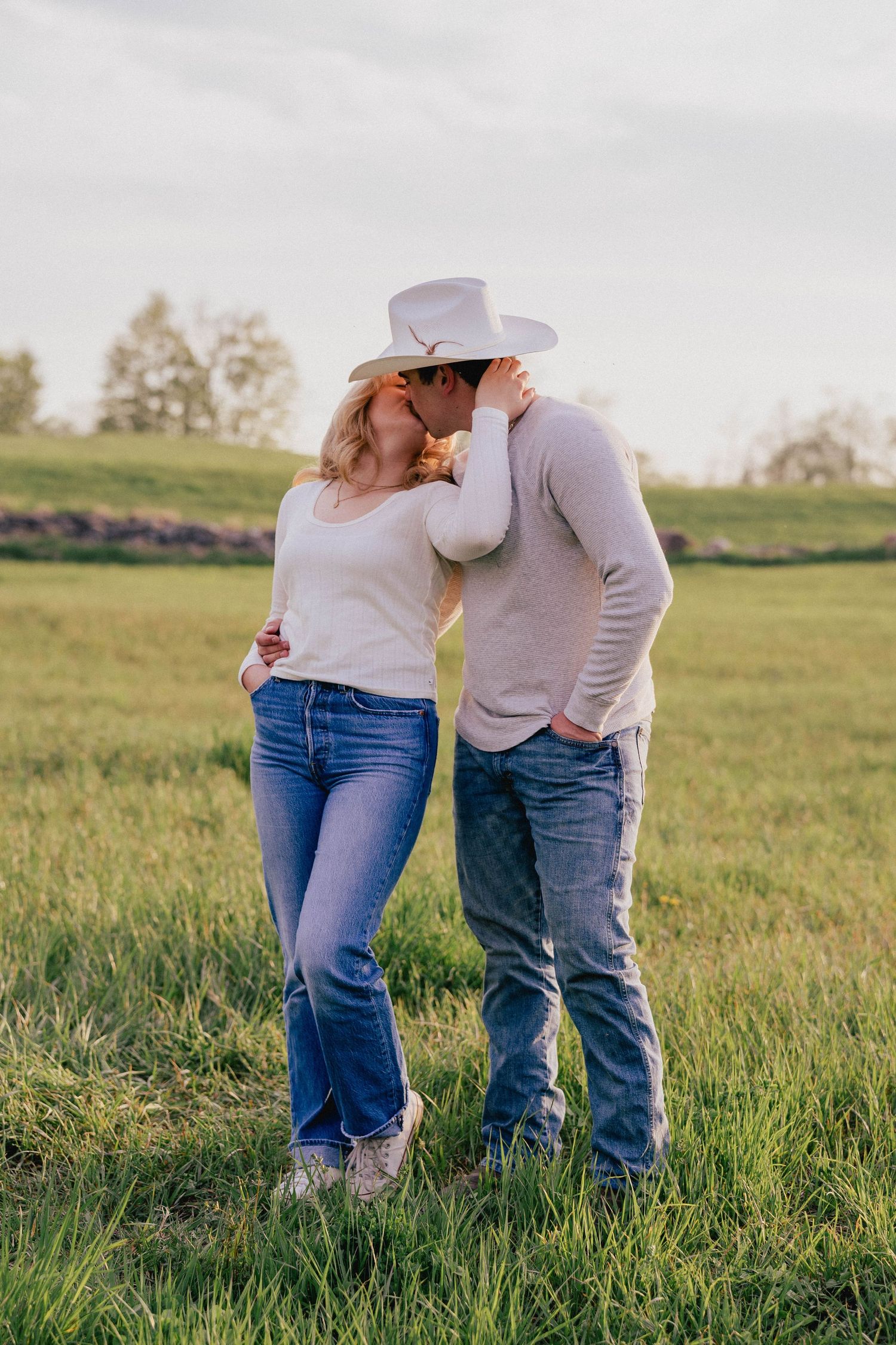 Couple sharing a tender kiss in a green field, man wearing a white cowboy hat.