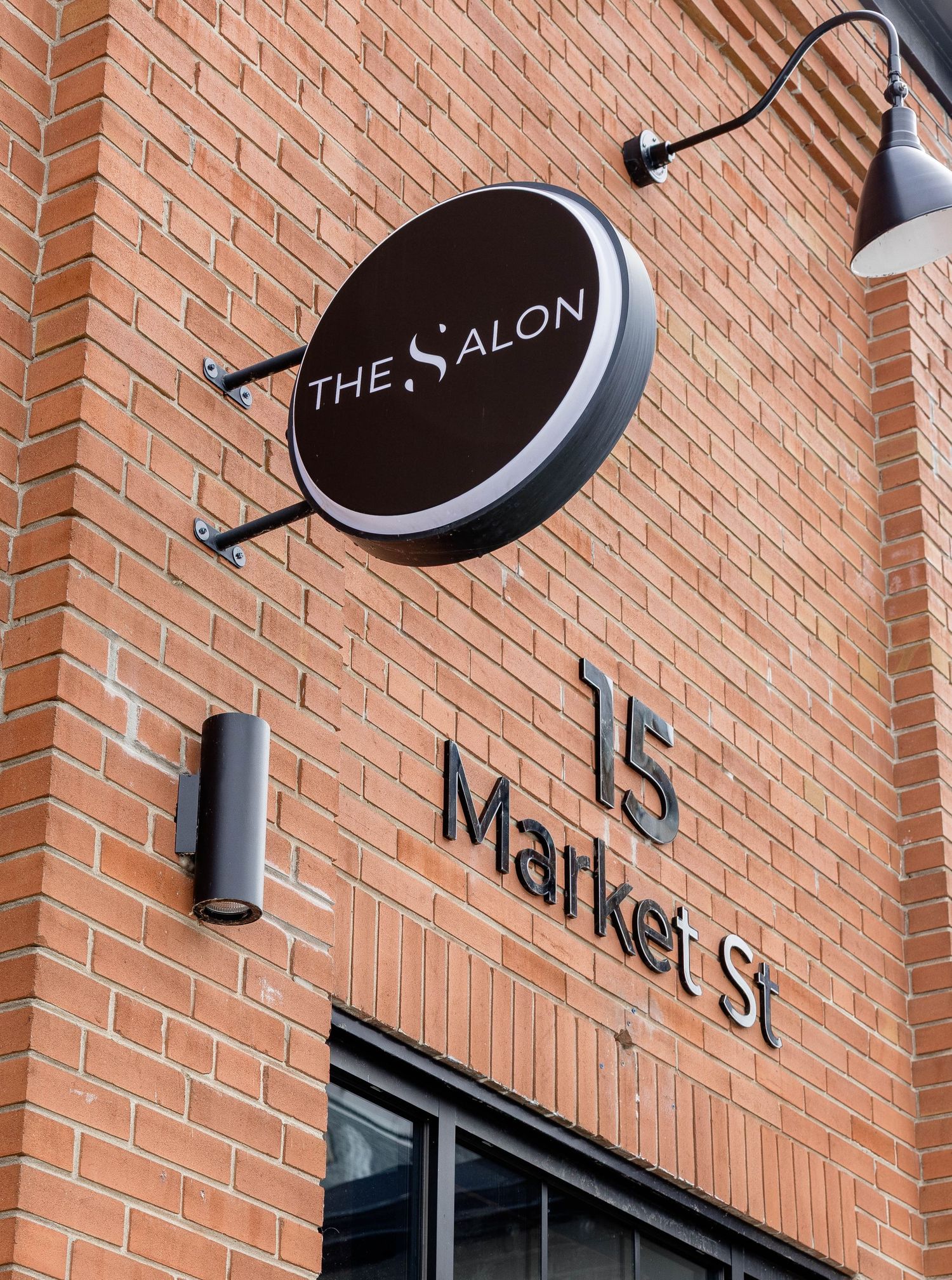 The Salon sign at 15 Market St, featuring a round dark brown logo on a brick building facade.