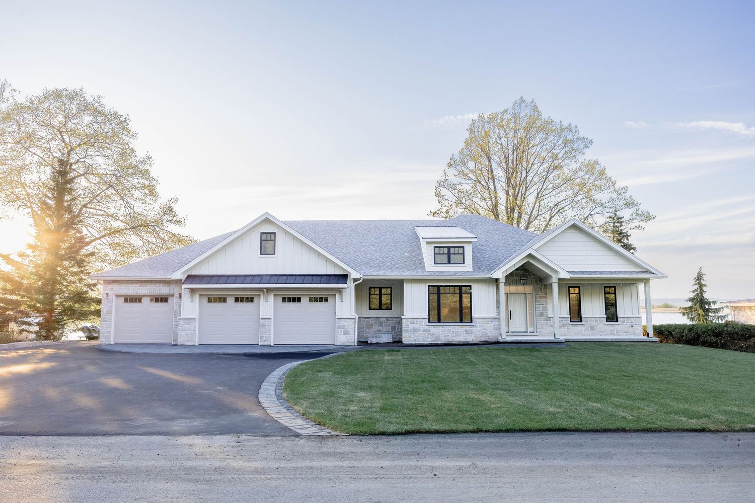 Modern white farmhouse exterior with three-car garage and lush green lawn at sunset.