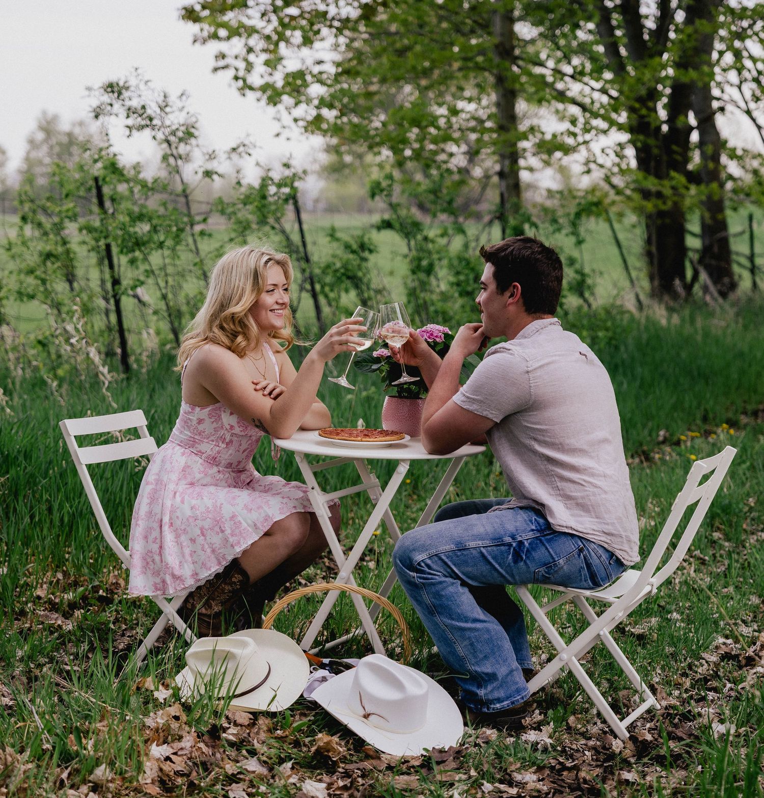 Couple toasting wine glasses at a white bistro table outdoors.