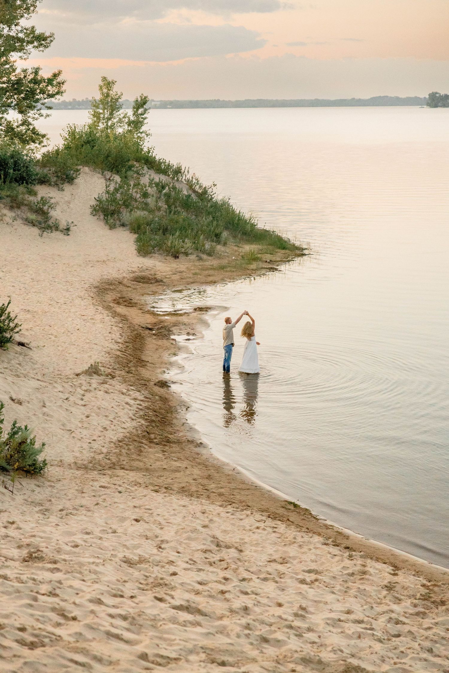 Couple dancing in shallow water at sandy beach during golden hour sunset.