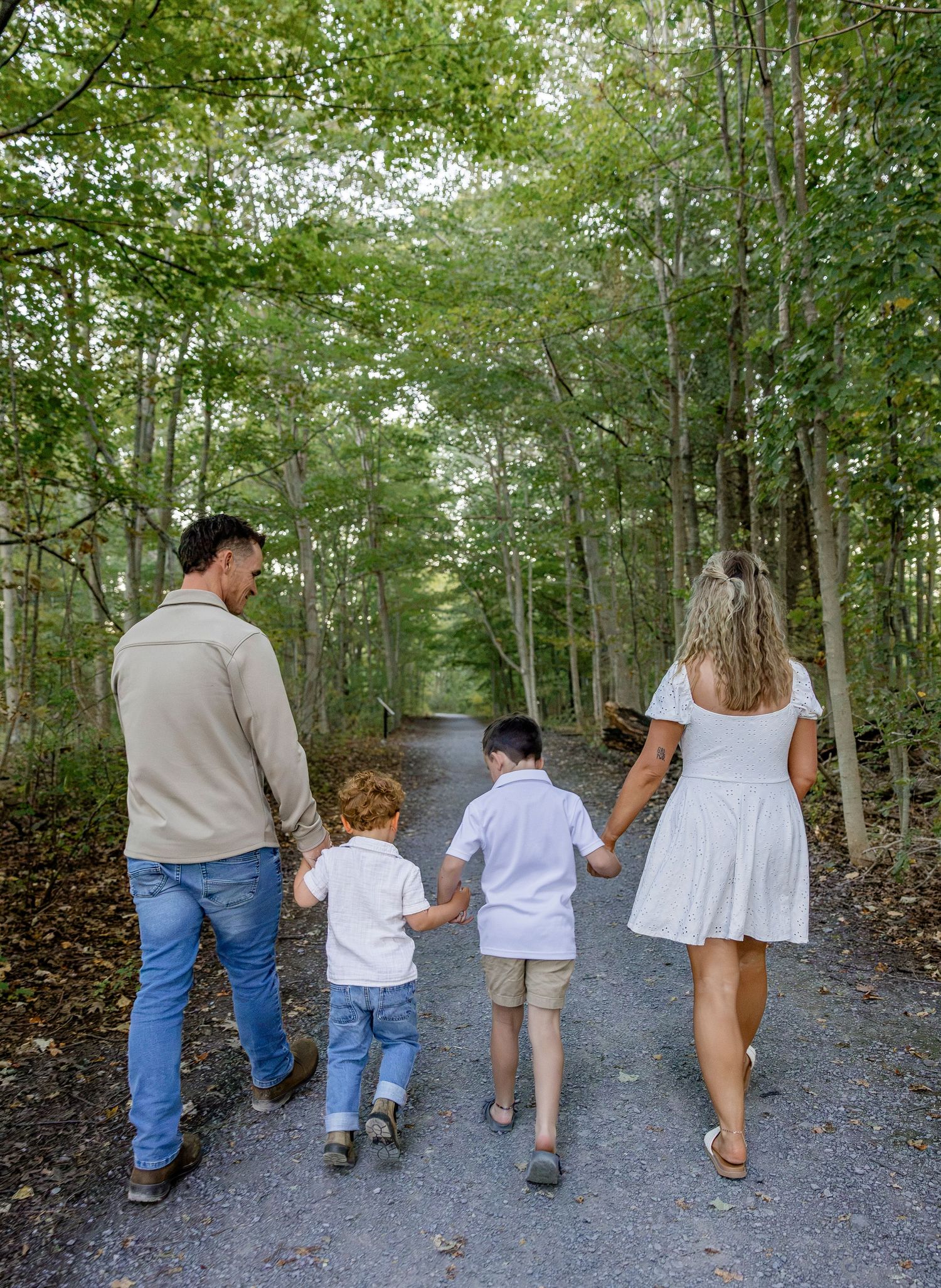 Family of four walking hand-in-hand down a tree-lined forest path in summer.