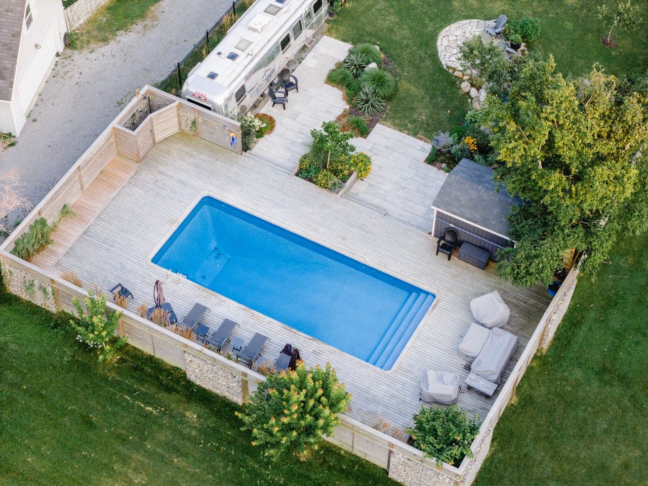 Aerial view of a rectangular backyard pool surrounded by stone decking, lounge chairs, and manicured greenery.