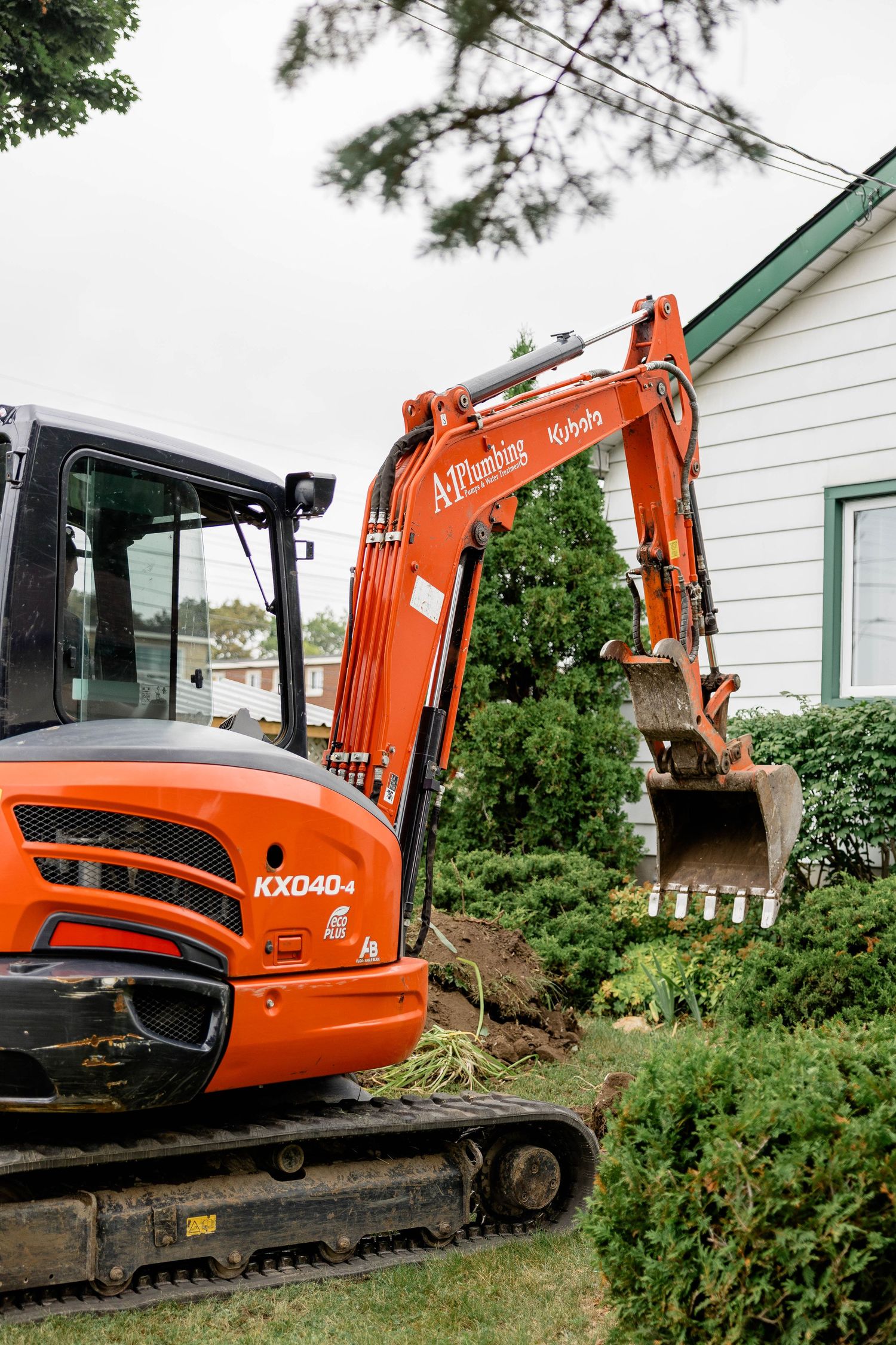Orange Kubota KX040-4 mini excavator working near a residential home, digging around shrubs and landscaping.