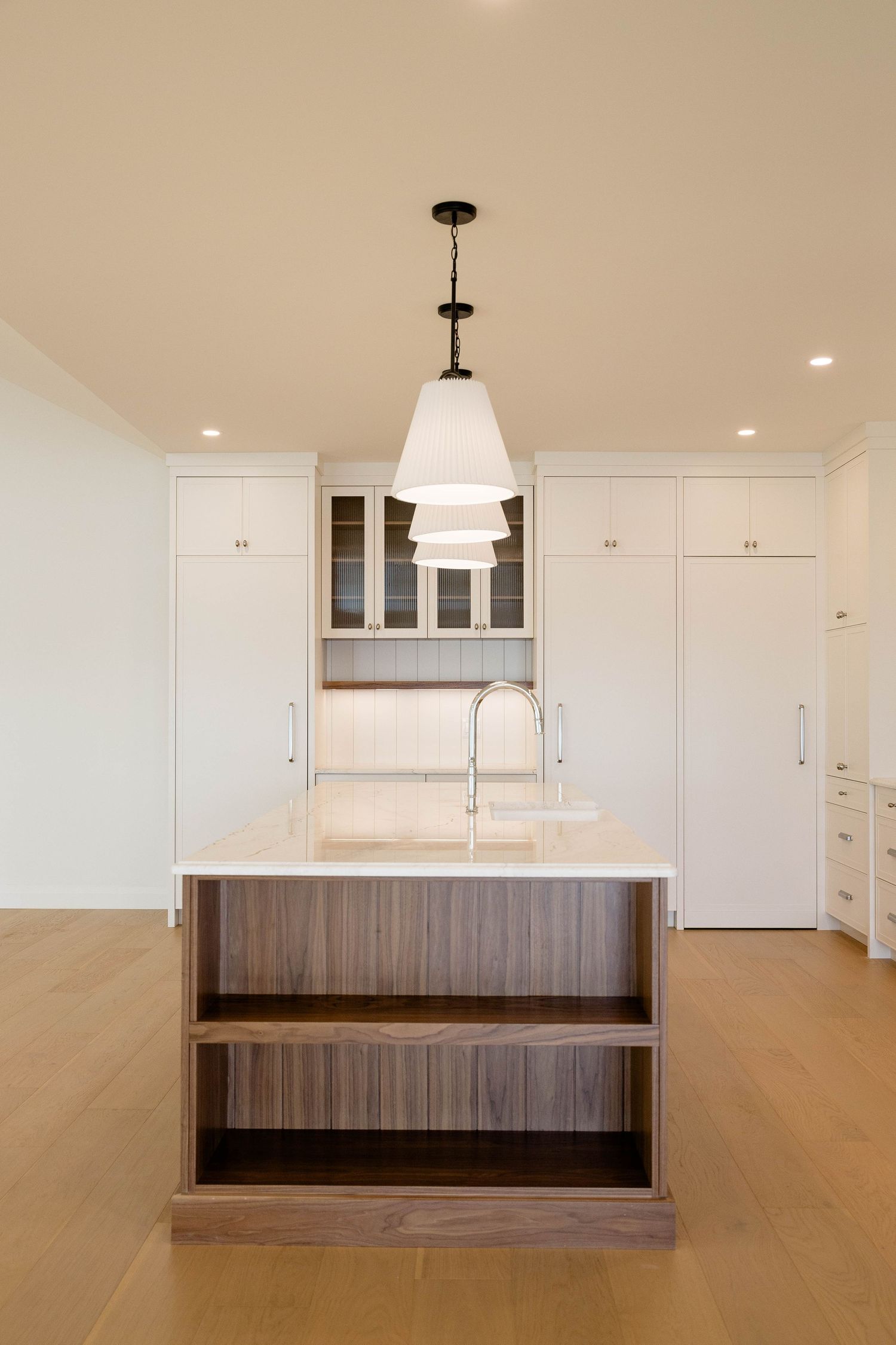 Minimalist kitchen island with walnut base, white countertop, pendant light, and surrounding white cabinetry.