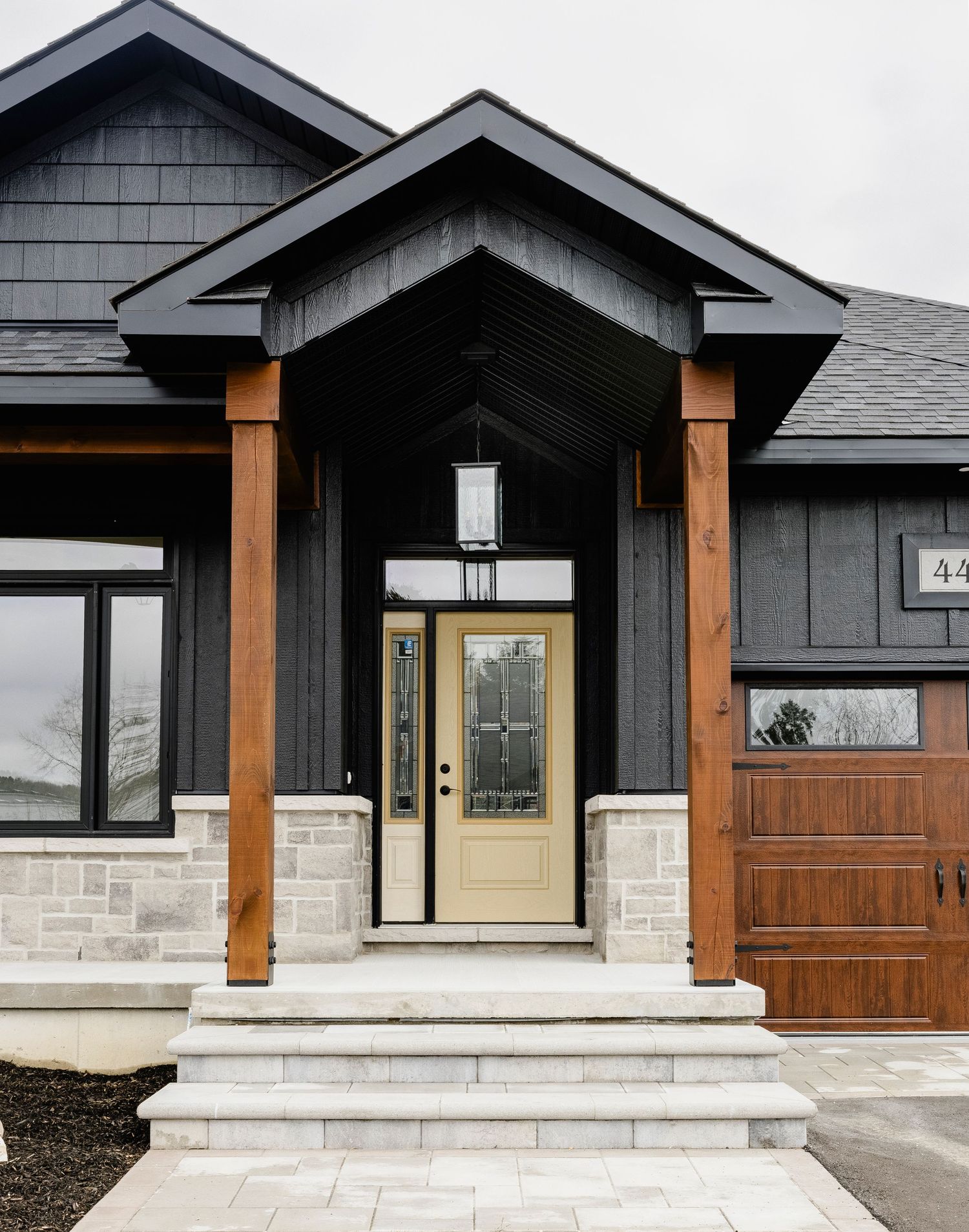 Close-up of craftsman home entrance with wood columns, cream front door, stone steps, and dark siding.