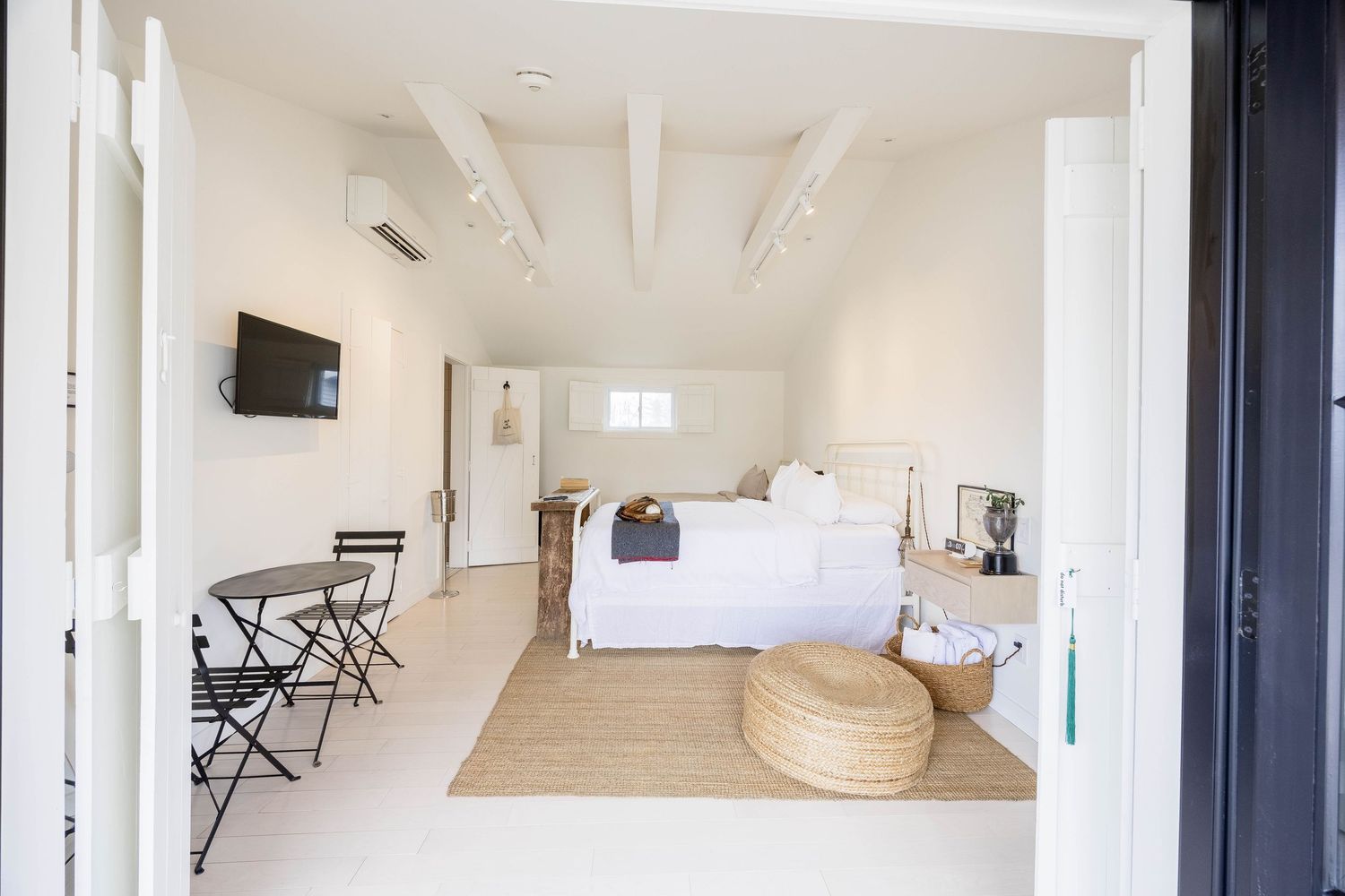 Bright minimalist bedroom suite with white walls, exposed beams, and neutral furnishings.