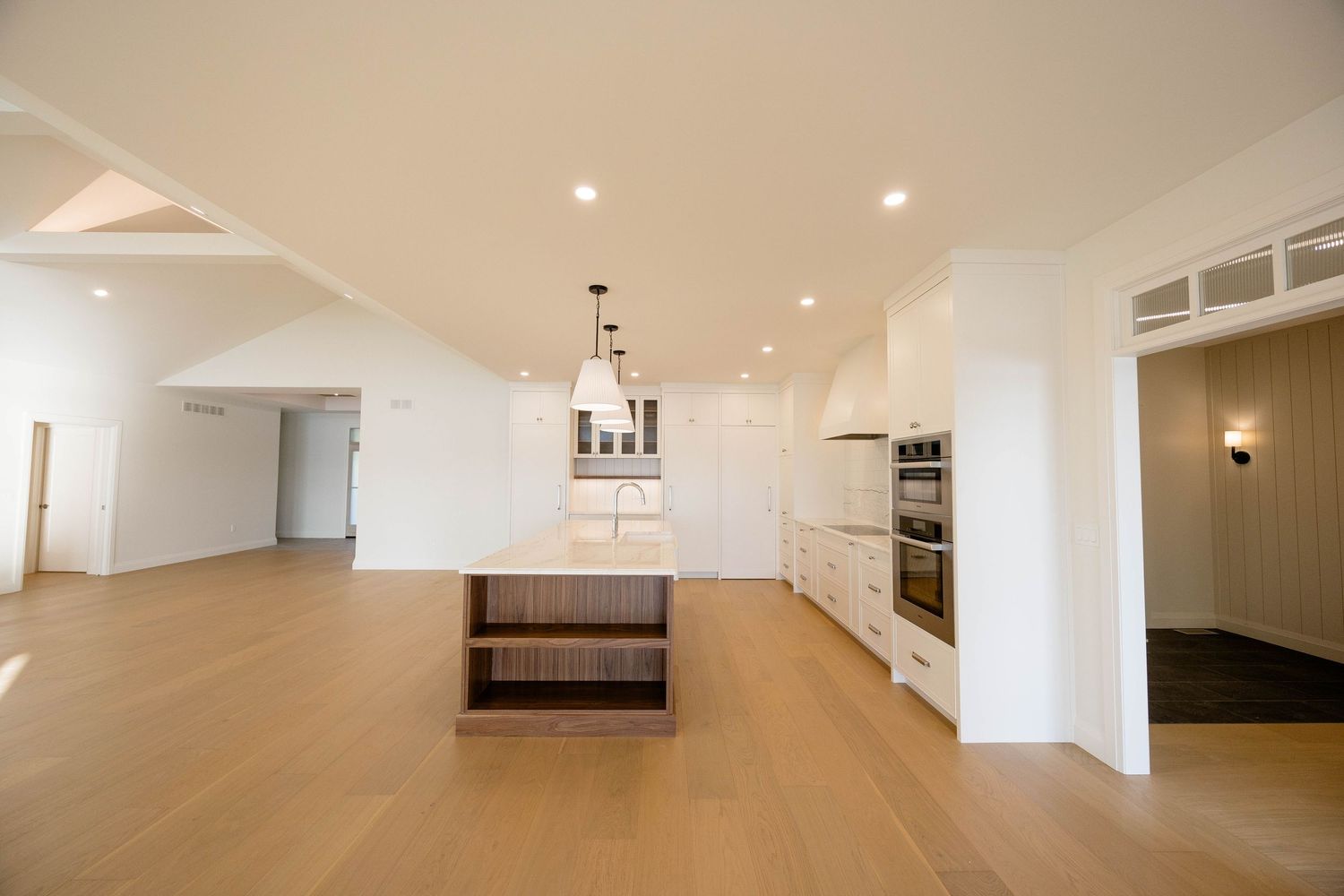 Modern kitchen with walnut island, white cabinetry, stainless steel ovens, and wide-plank light hardwood flooring.
