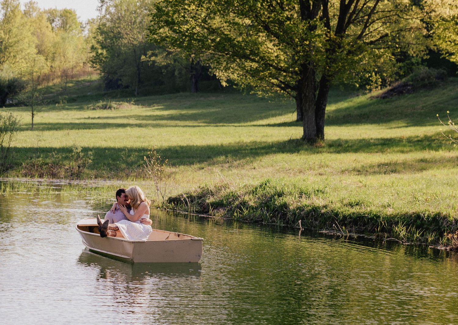 Couple sharing a romantic moment in a small boat on a serene pond with trees.