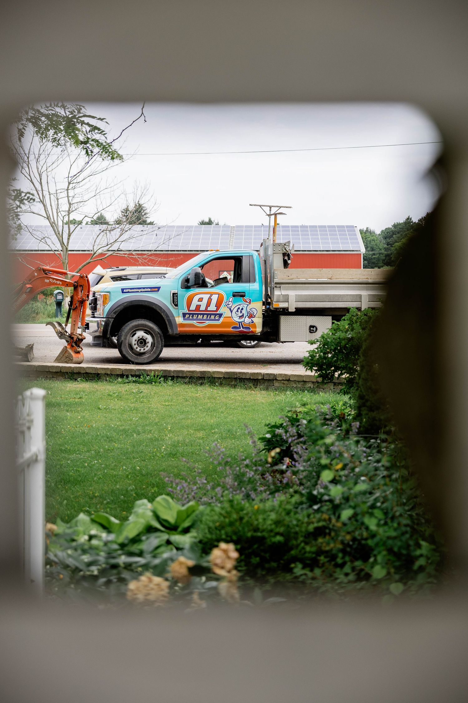 A1 Plumbing branded truck viewed through a fence gap near a home.