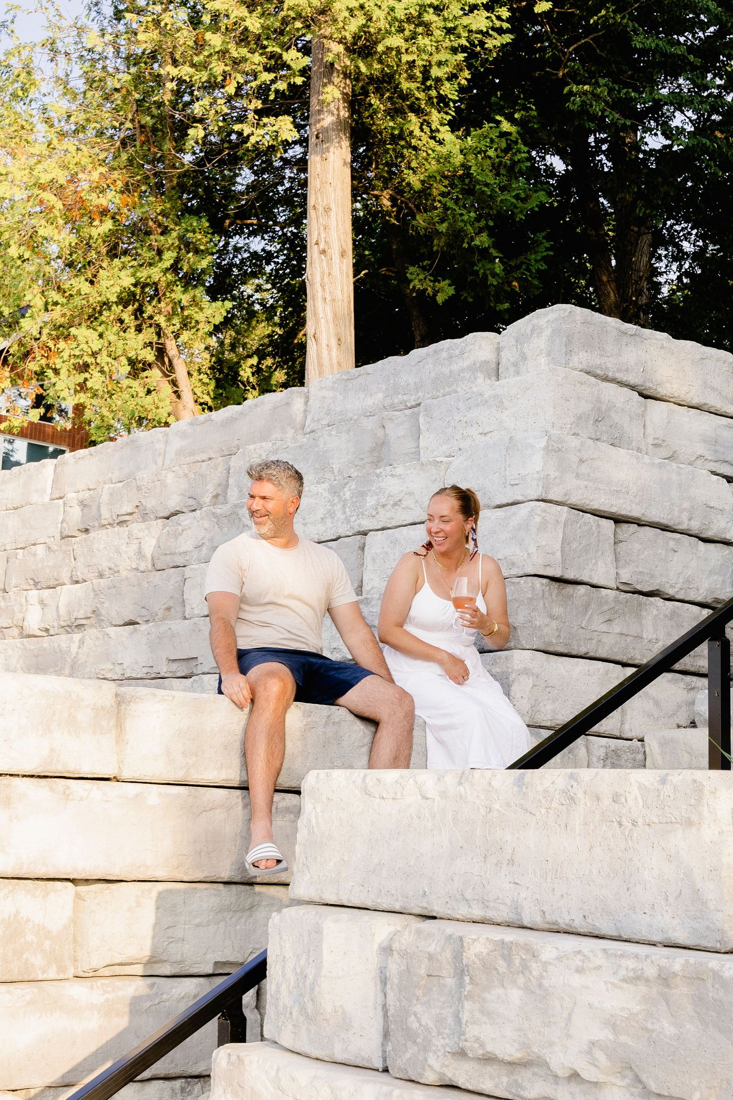 Happy couple relaxing on stone steps outdoors, surrounded by lush green trees in summer.
