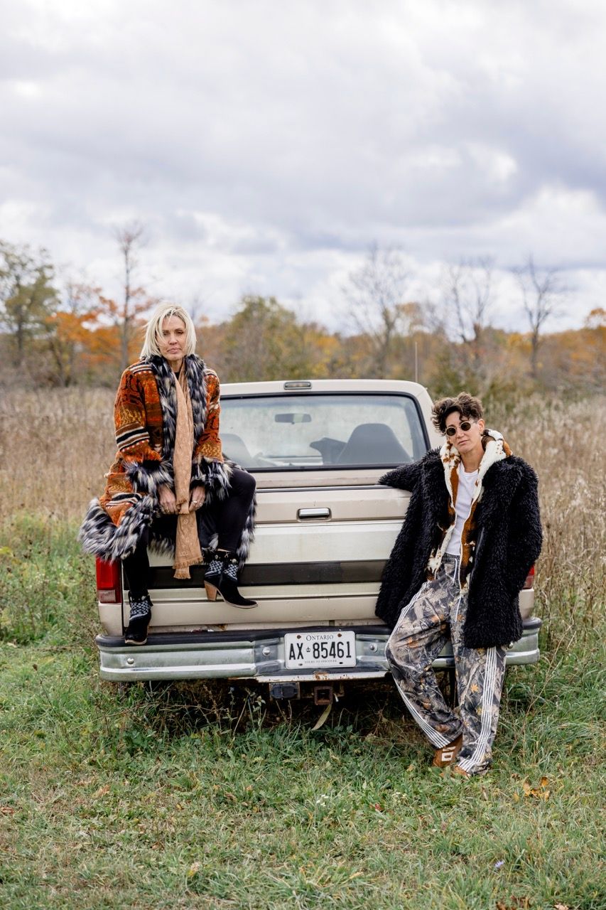 Two women in boho-chic fall fashion posing at the back of a vintage beige Ford pickup truck.
