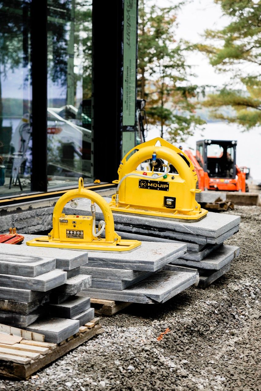 Two yellow MQUIP vacuum lifters resting on stacked stone slabs at an outdoor construction site.