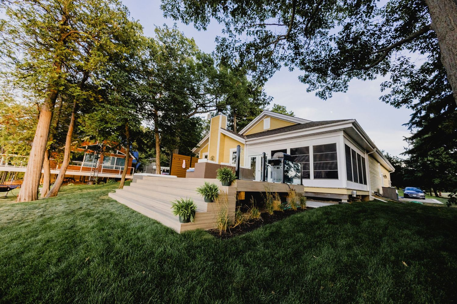 Charming yellow cottage-style home with a new wooden deck surrounded by mature trees on green lawn.