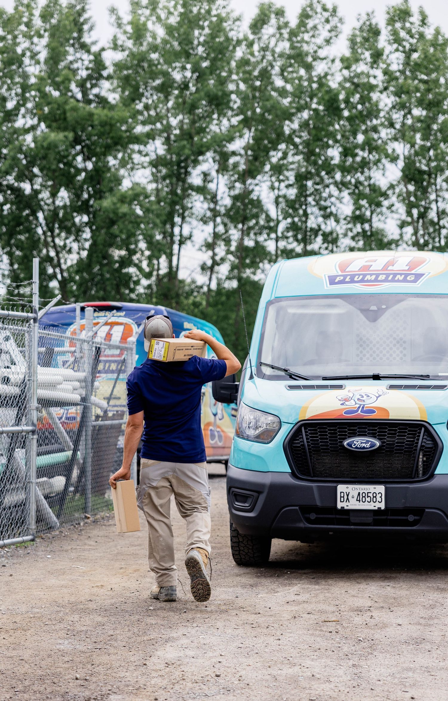 A1 Plumbing technician carrying boxes toward a branded Ford Transit service van outdoors.