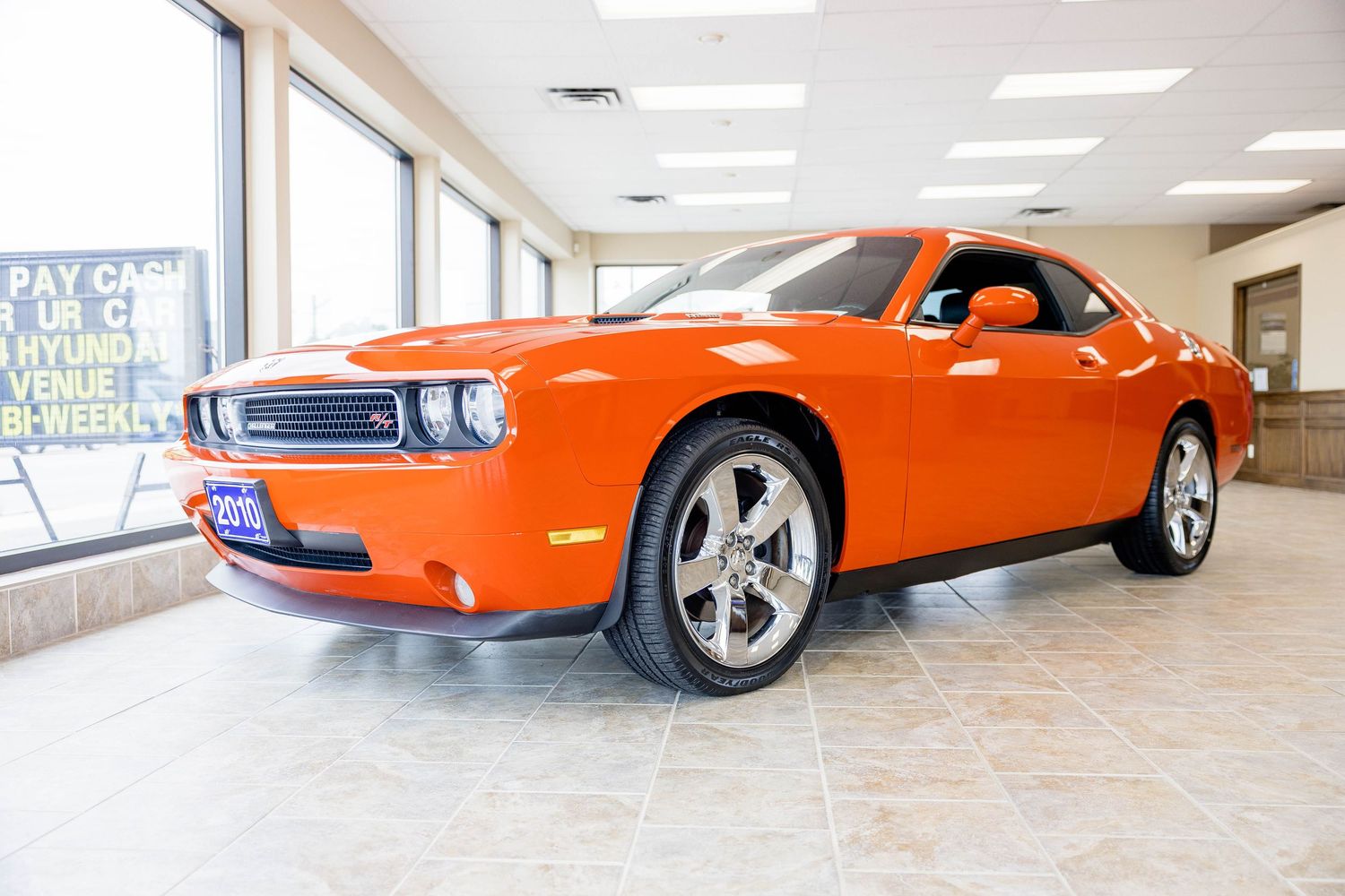 Bright orange Dodge Challenger muscle car displayed inside a car dealership showroom.