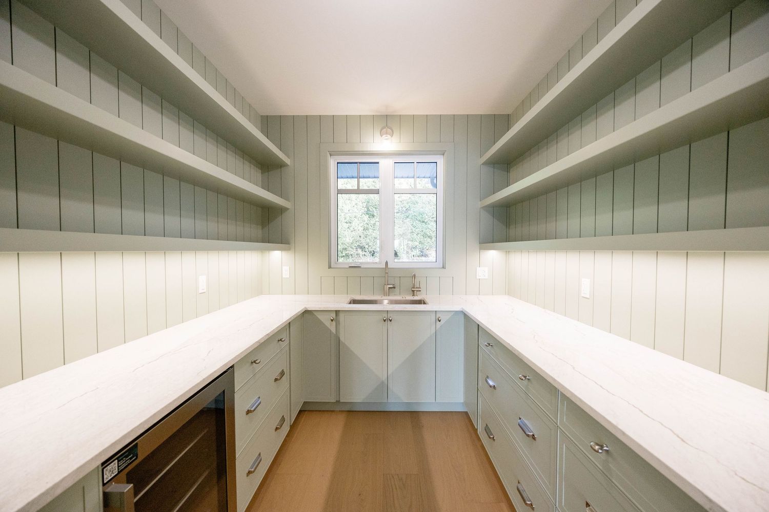 Spacious walk-in pantry with sage green shaker cabinets, white quartz countertops, and open shelving.