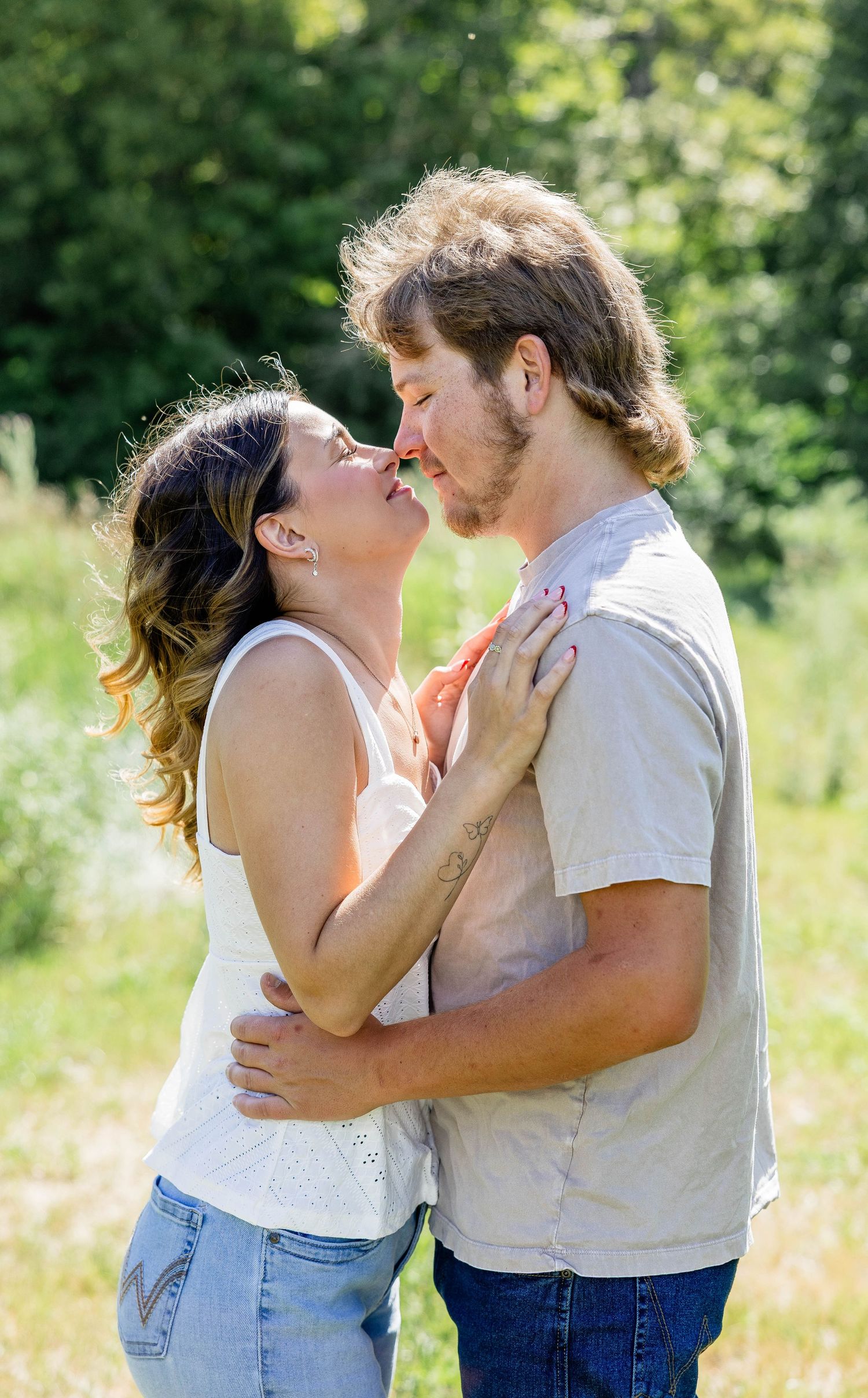 A couple sharing a romantic moment about to kiss in a sunny green meadow outdoors.