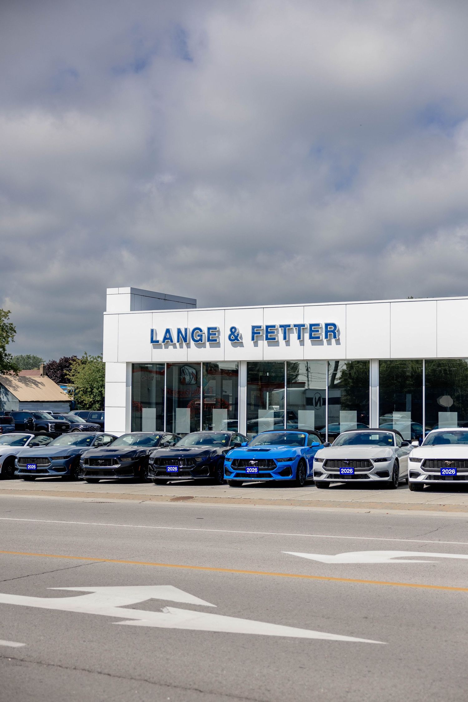 Lange & Fetter Ford dealership exterior with a row of new Ford Mustangs on display under a cloudy sky.