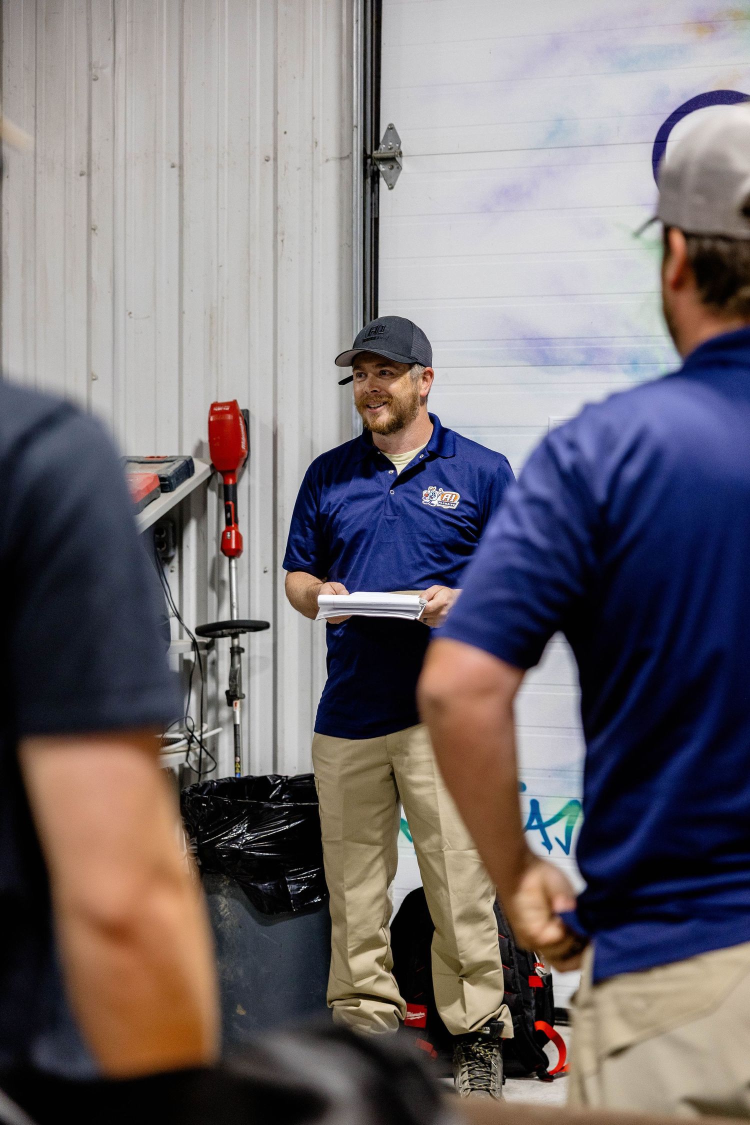 Plumbing team supervisor holding documents during an outdoor staff briefing at a warehouse.