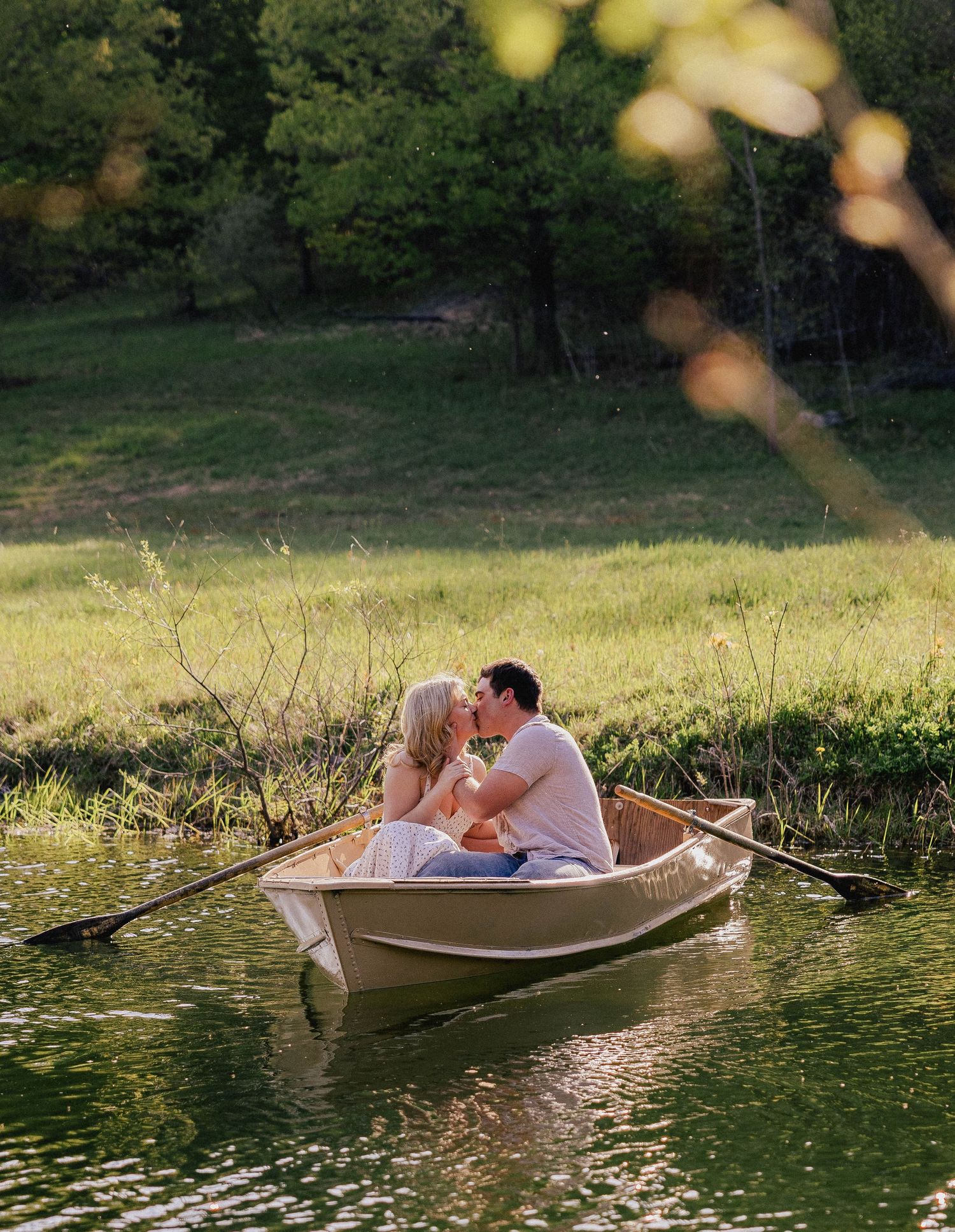 Couple sharing a romantic kiss in a rowboat on a calm pond.