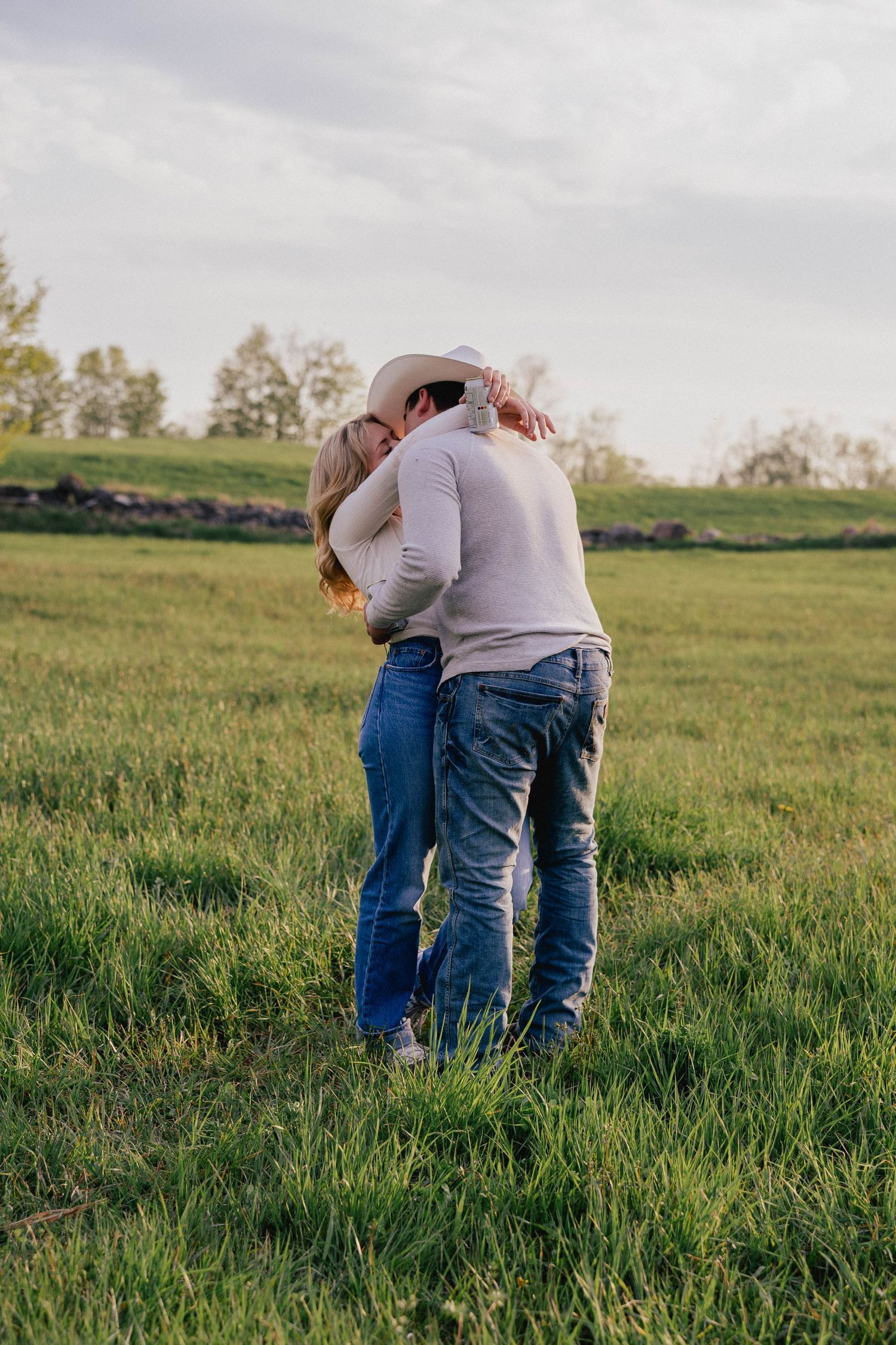 Couple in jeans embracing and kissing in a green meadow under a cloudy sky.