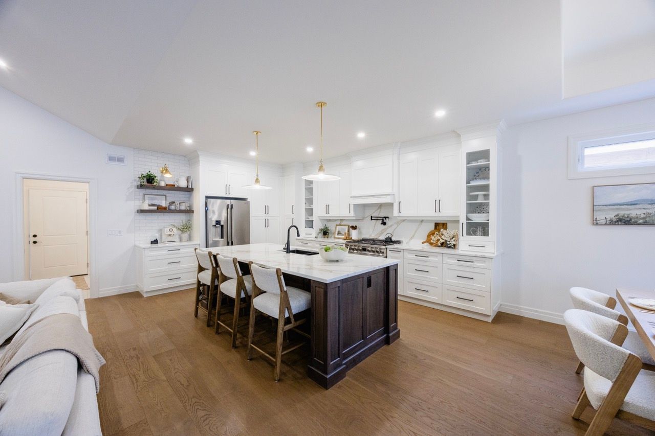 Modern open-concept kitchen with white cabinets, dark island, pendant lights, and hardwood floors in a bright home.