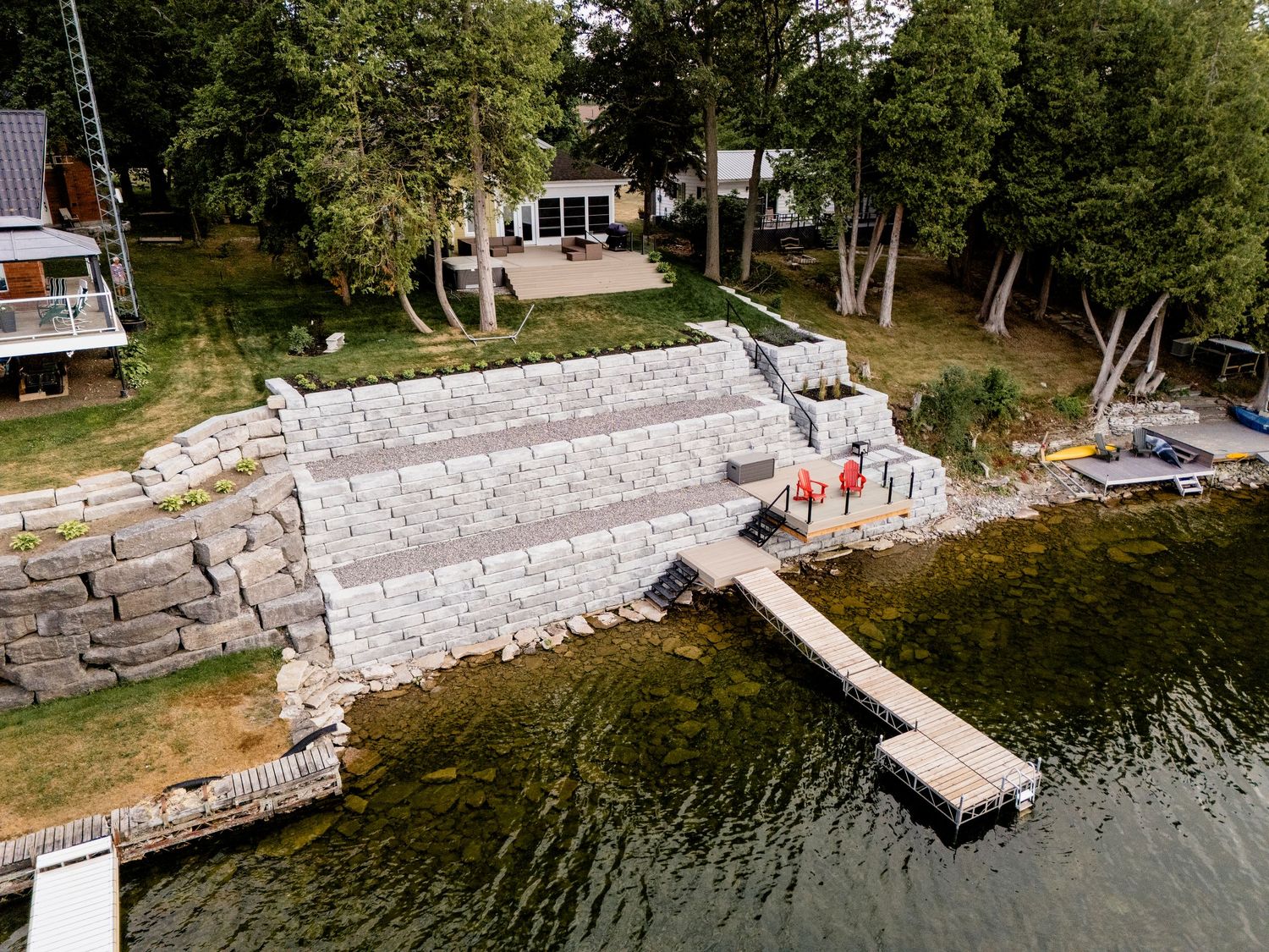 Aerial view of a stone retaining wall terraced waterfront property with a dock on a lake.