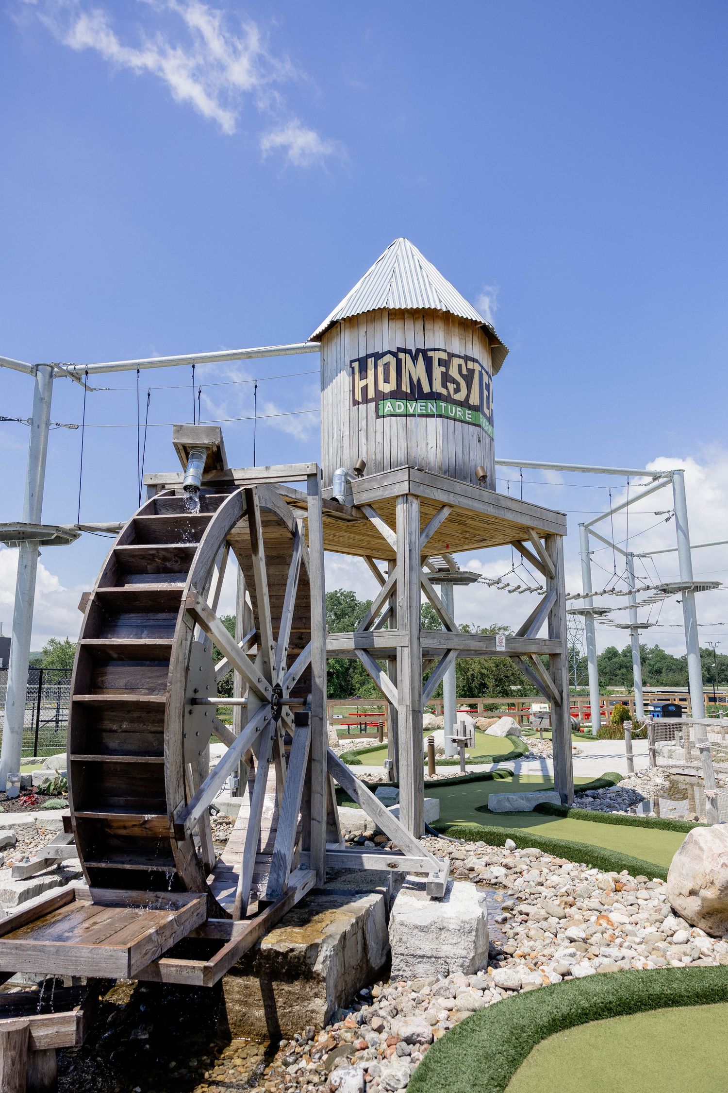 Homestead Adventures mini golf course featuring a rustic water wheel and wooden tower.