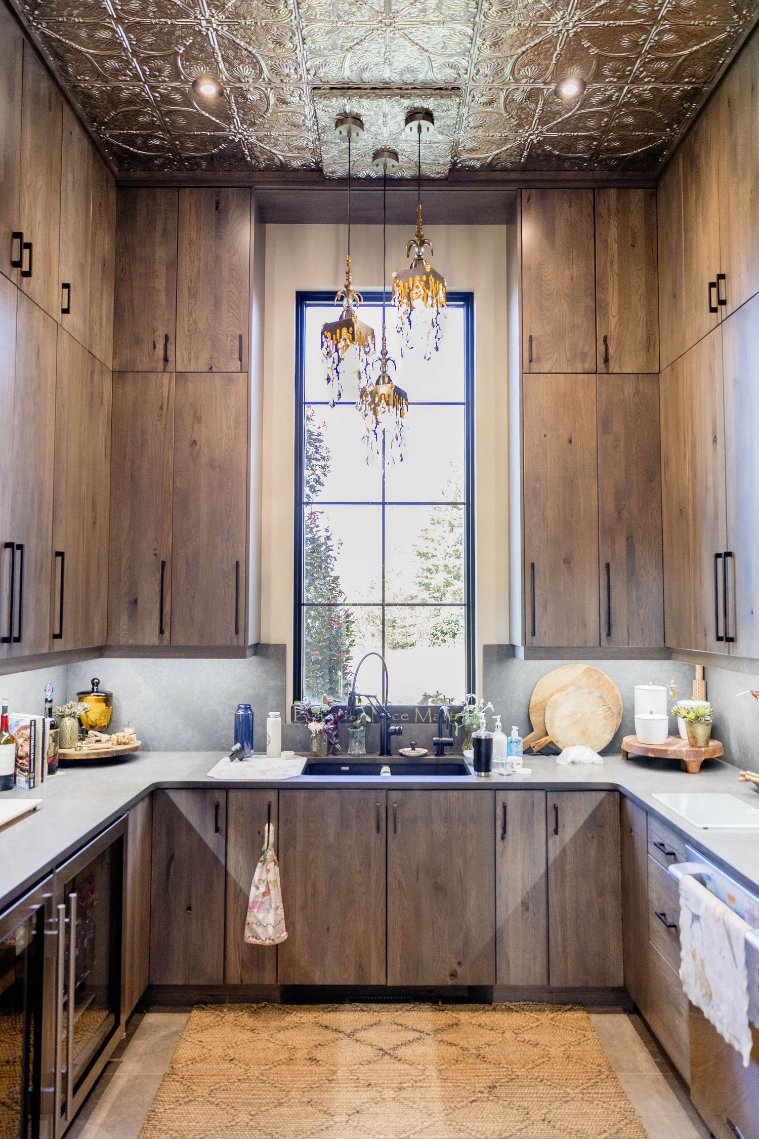 Elegant butler pantry with dark wood cabinets, white countertops, ornate tin ceiling, and tall window.