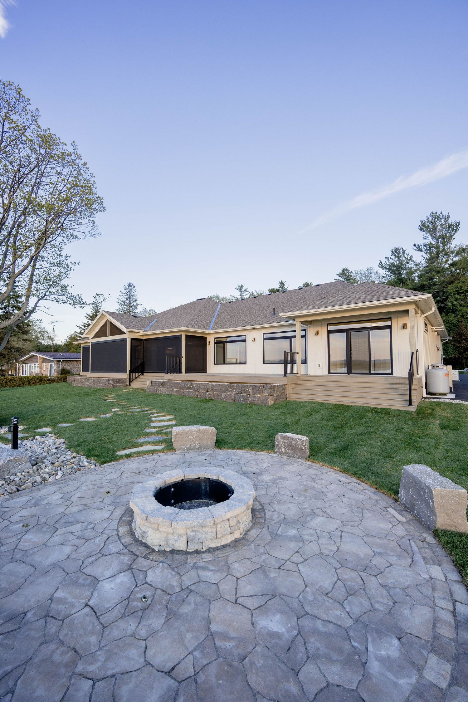 Backyard patio with stone fire pit, stamped concrete, deck, and screened porch at twilight.