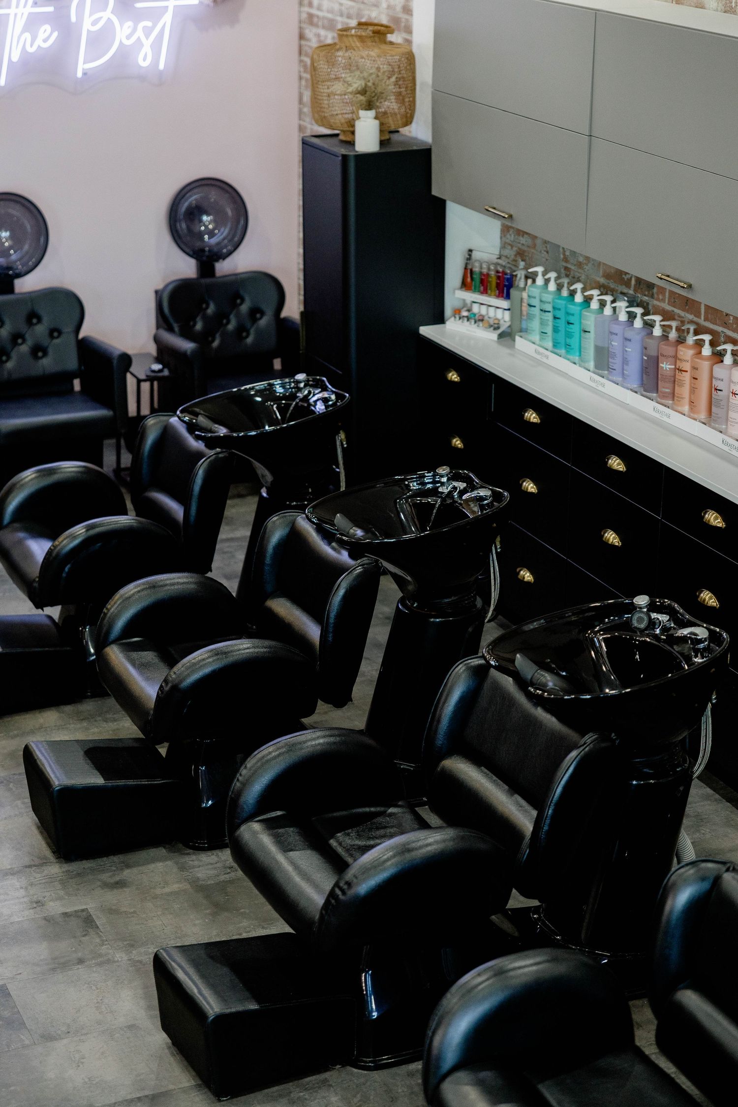 Luxury black leather shampoo bowls and wash chairs lined up in a modern hair salon with product display.