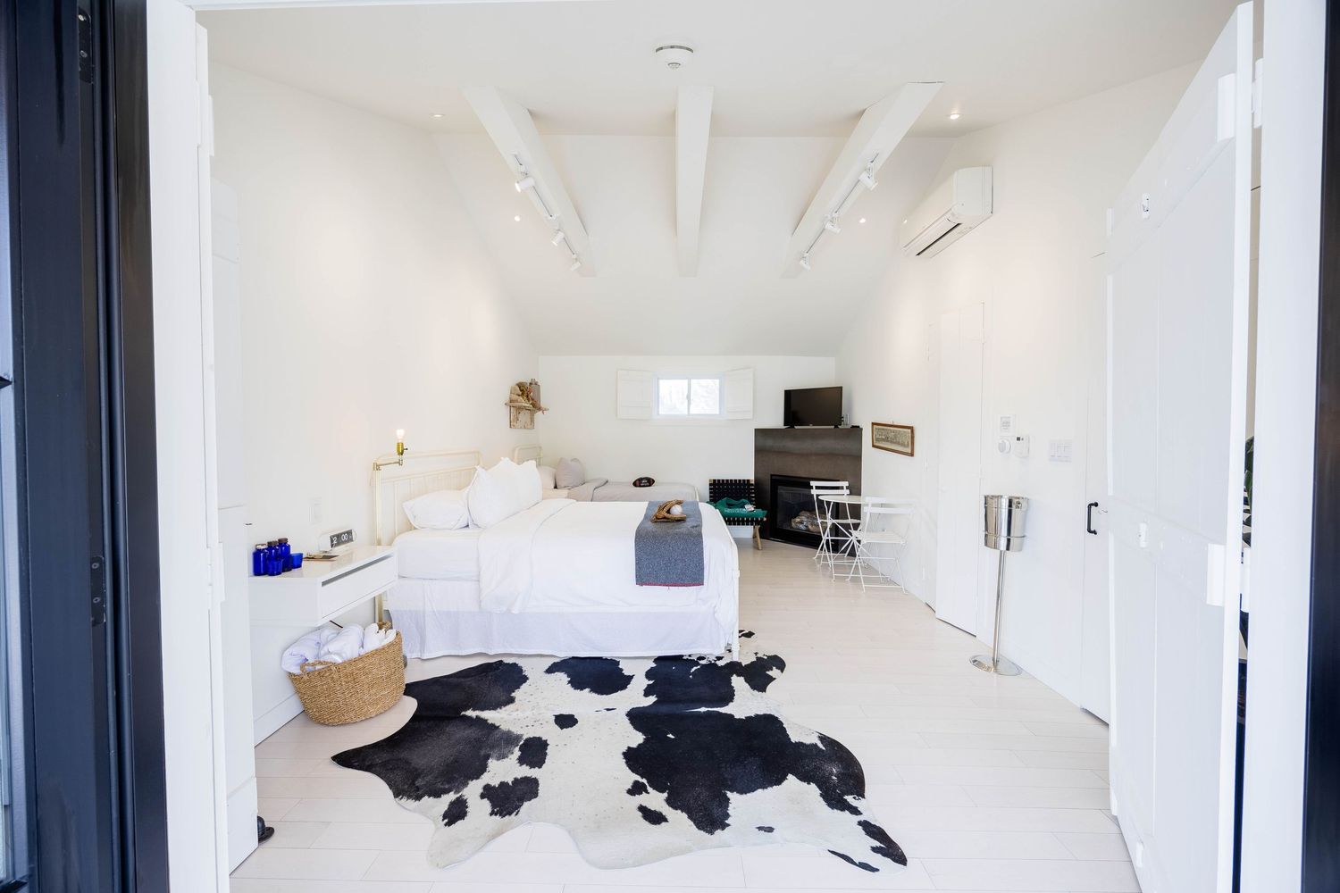 Bright white studio bedroom with exposed beam ceiling, cowhide rug, and minimalist decor.