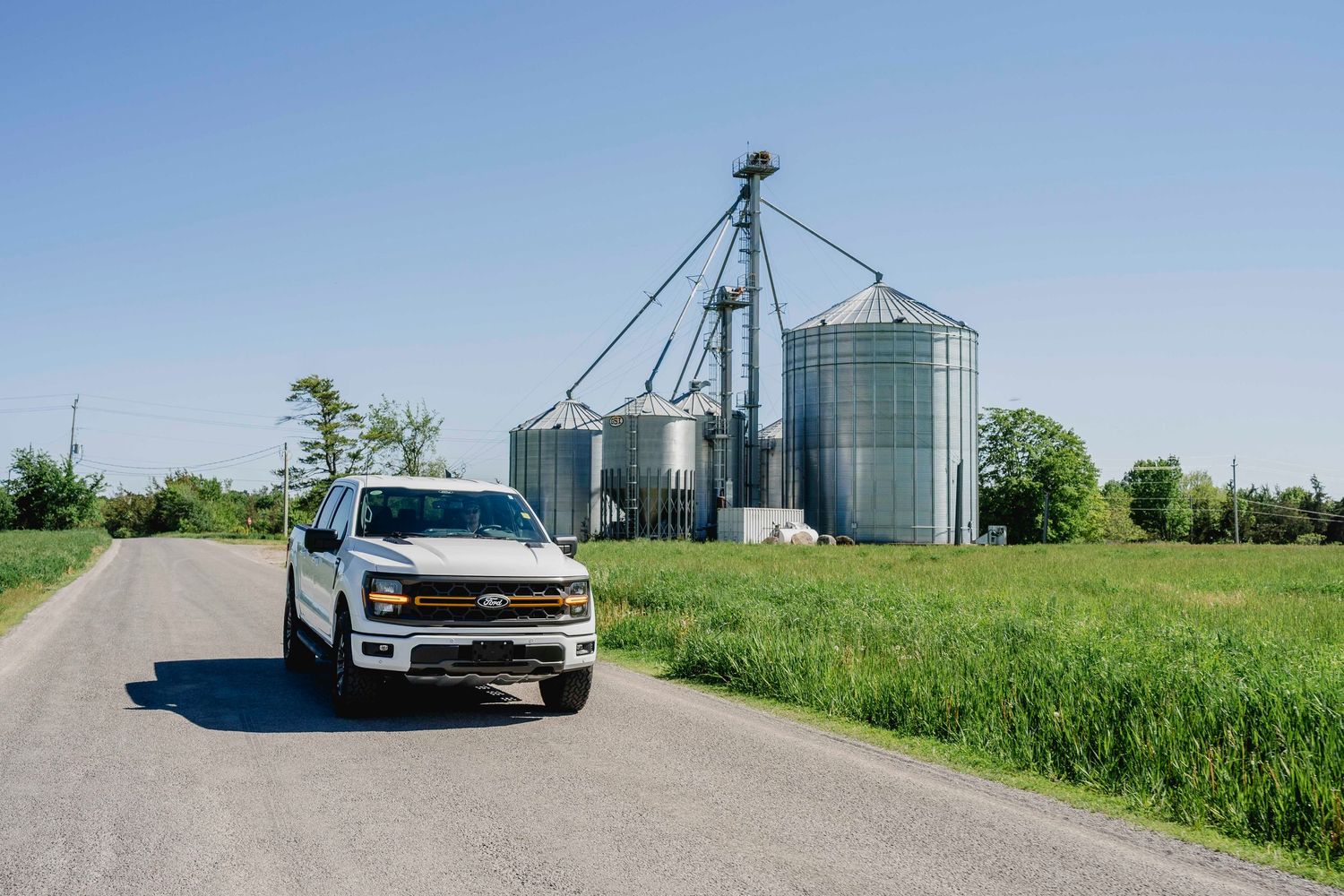 White Chevrolet Silverado truck parked on a country road with large grain storage silos behind it.
