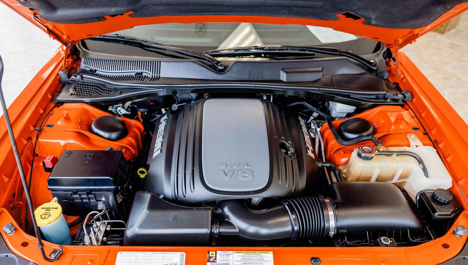 Close-up of an orange Dodge Challenger V8 engine under an open hood showing detailed components.