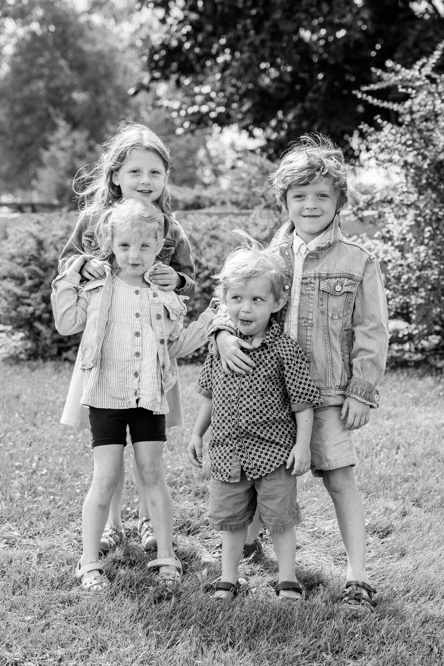 Black and white portrait of four young children posing together outdoors in a garden.