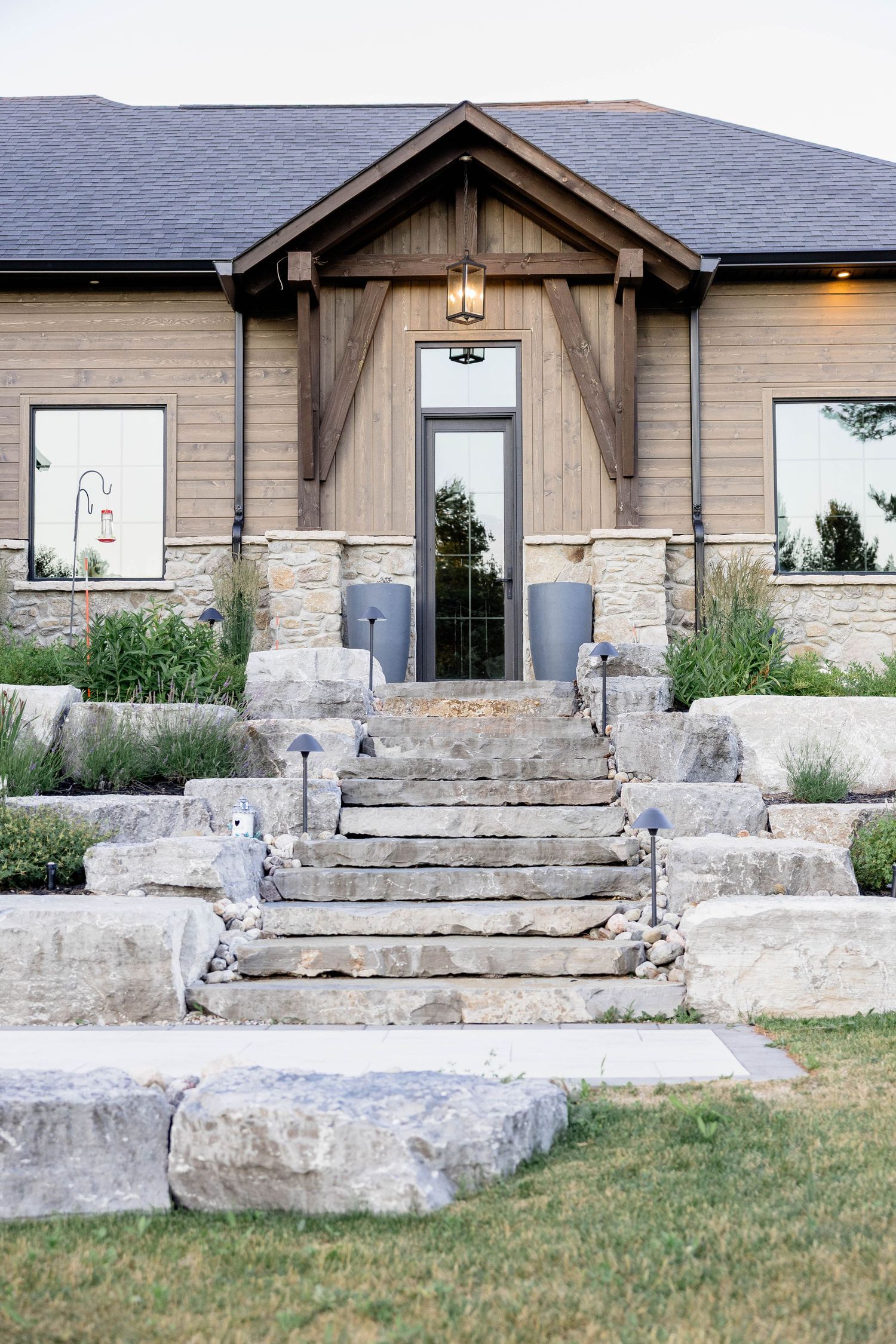 Stone steps lead to a rustic craftsman home entrance with natural wood accents and boulder landscaping.